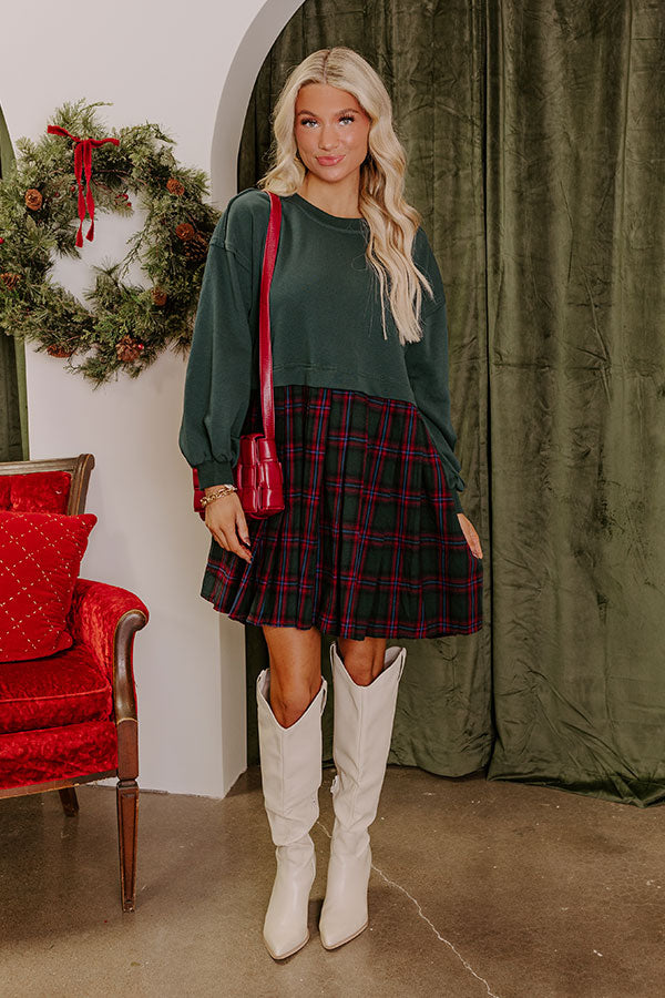 Cozy winter outfit featuring a green sweater top and plaid skirt paired with chic white boots.