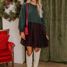 Cozy winter outfit featuring a green sweater top and plaid skirt paired with chic white boots.