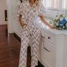Woman wearing a white floral jumpsuit with short sleeves and a tie waist, styled with white ankle boots for a chic winter look.